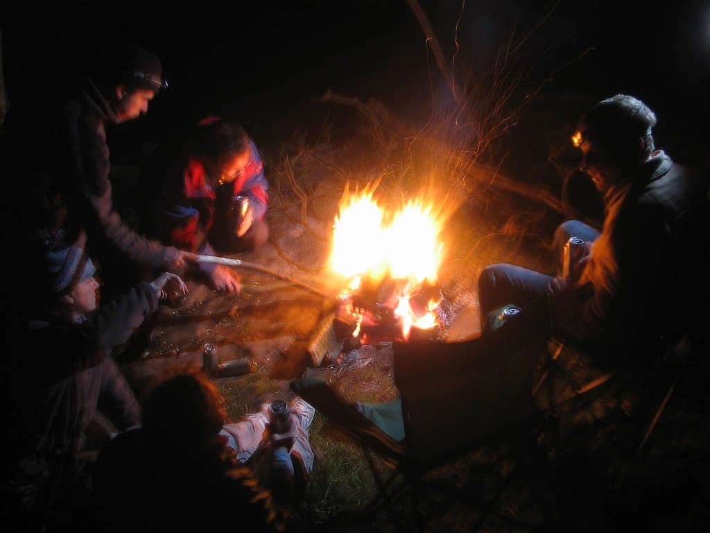 A folding camp chair set up beside a campfire