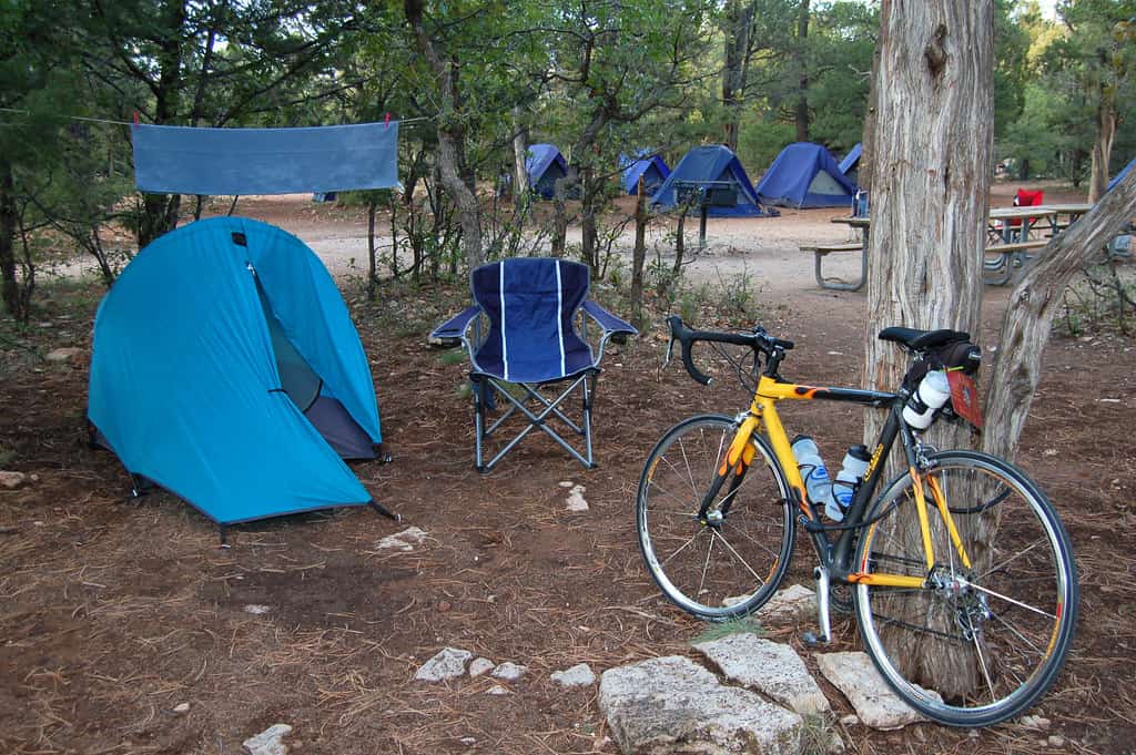 A tent pitched beside a parked car at a campground