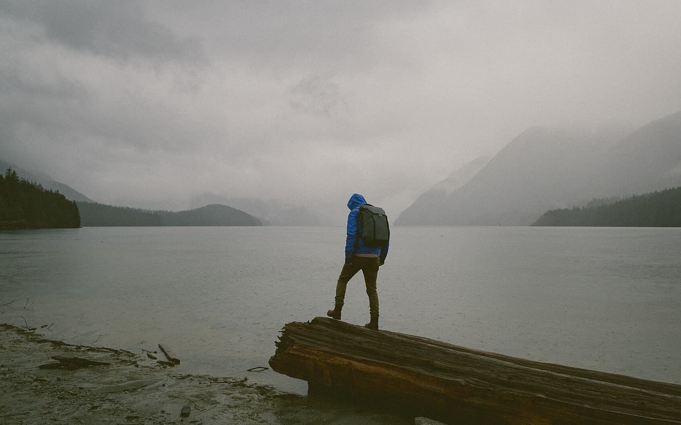 A hiker in a blue rain jacket beside a lake in heavy weather